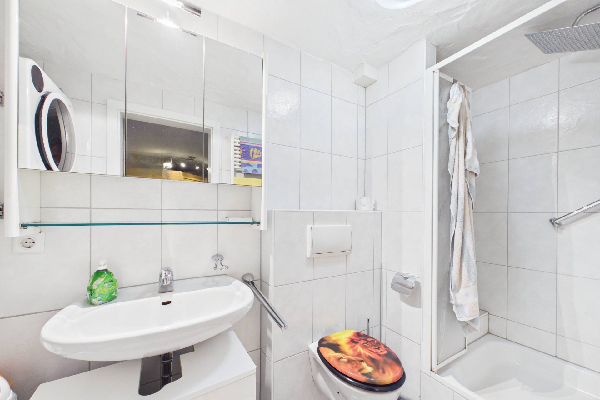 Kleines Badezimmer mit Dusche, WC, Waschbecken und Spiegel. Handtuch hängt an der Dusche.