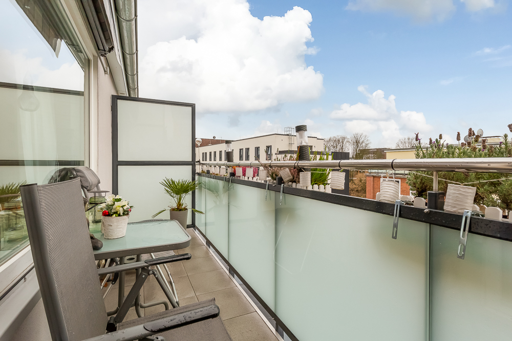 Moderner Balkon mit zwei Stühlen, Glastisch, Pflanzen und Sichtschutz aus Milchglas.