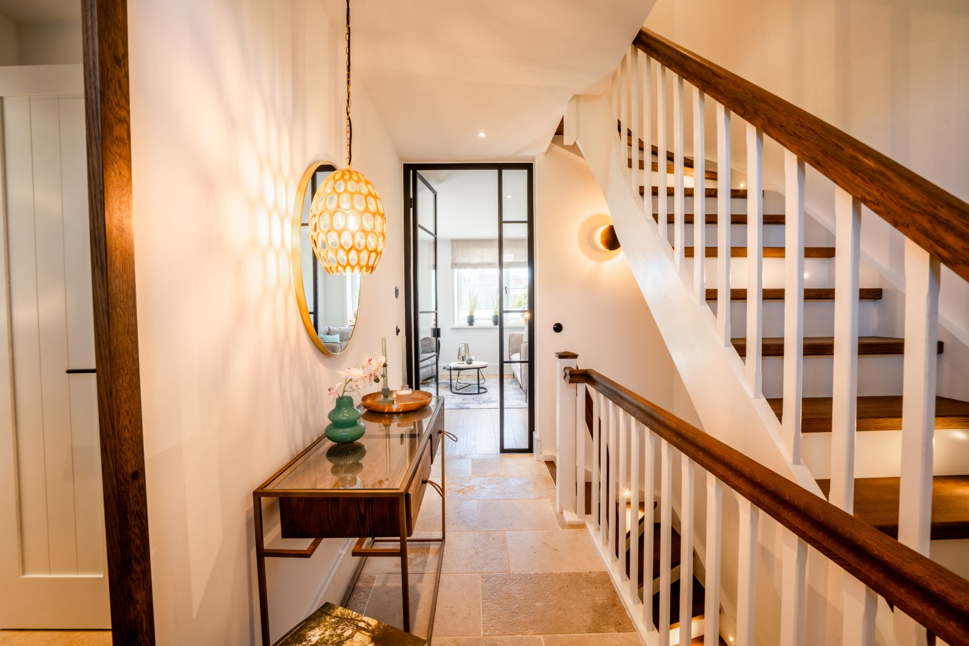 Heller Flur mit Treppe, Spiegel, Tisch und Dekoration, Blick in ein Wohnzimmer.
