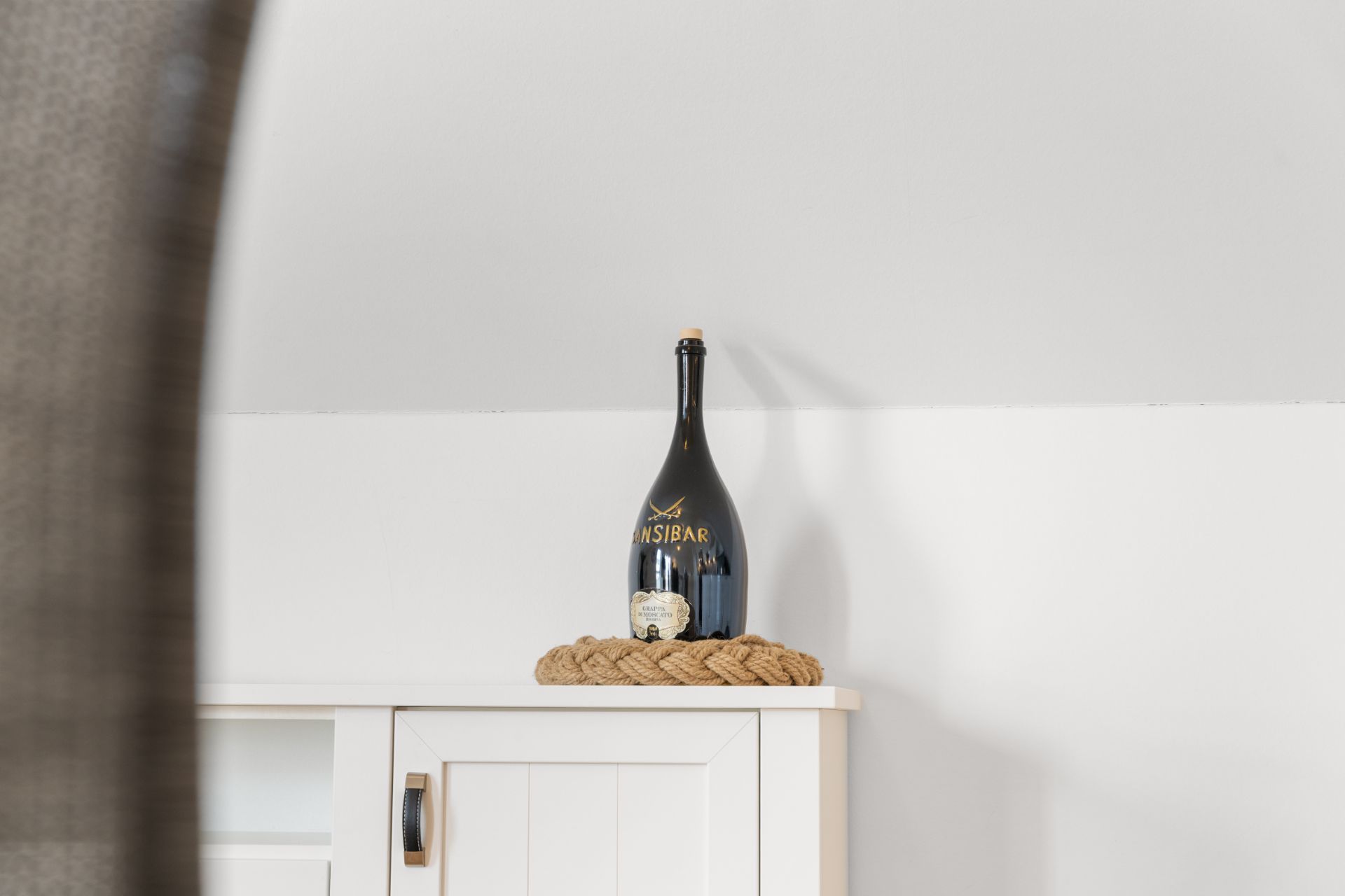 Große schwarze Flasche steht auf einem weißen Schrank, dekoriert mit geflochtenem Seil.