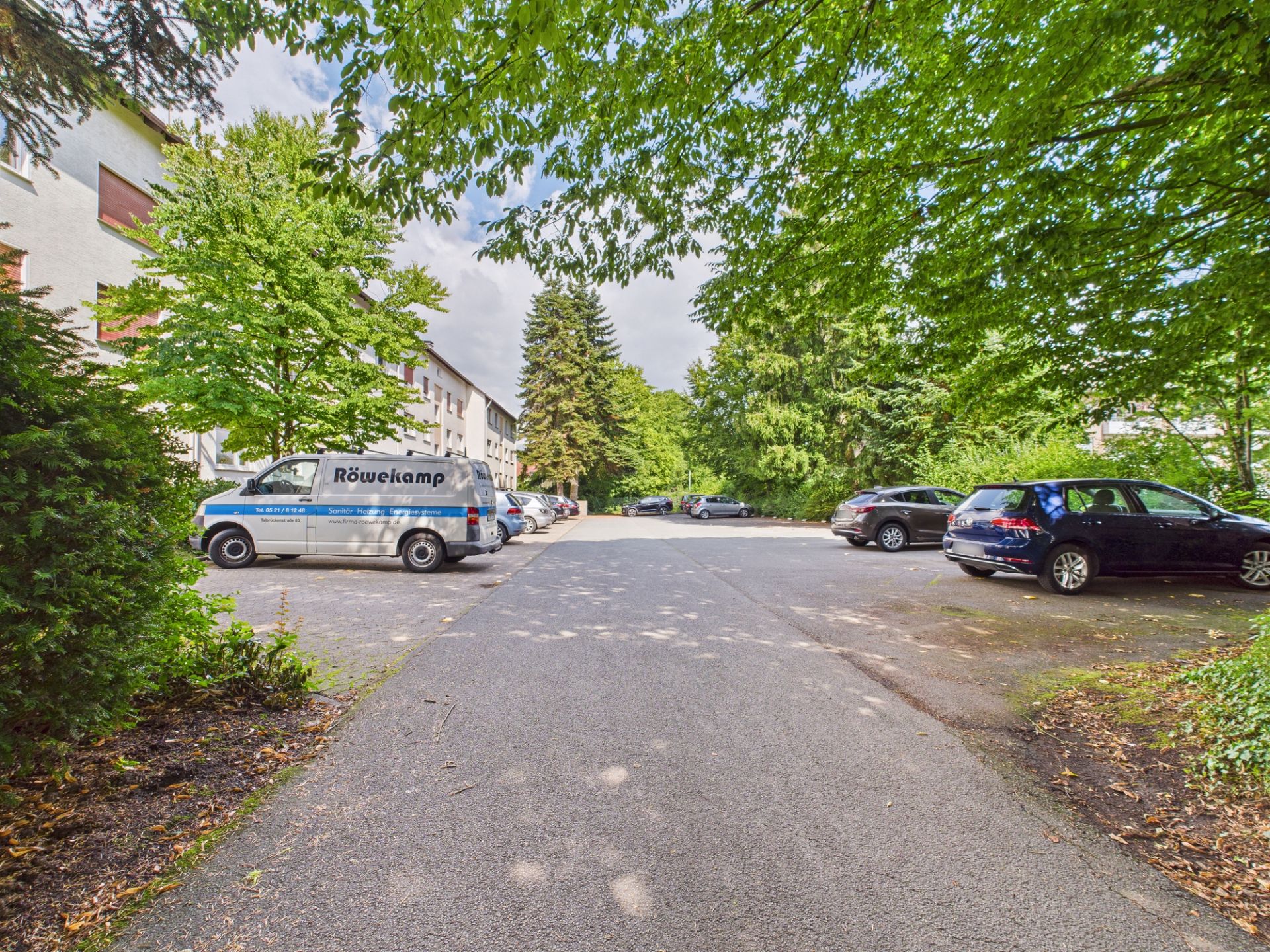 Wohnparkplatz mit mehreren Autos und Bäumen an den Seiten.