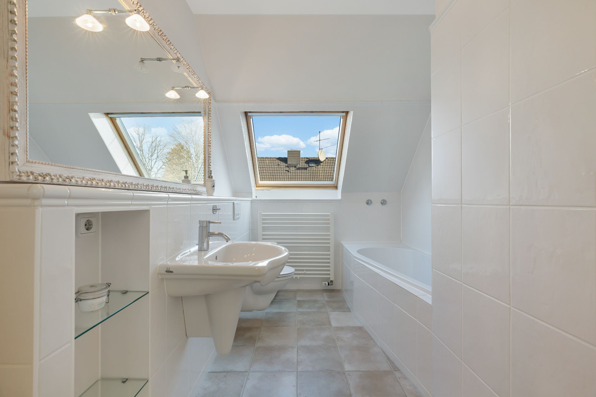 Helles Badezimmer mit Dachfenstern, Waschbecken, Spiegel und Badewanne.