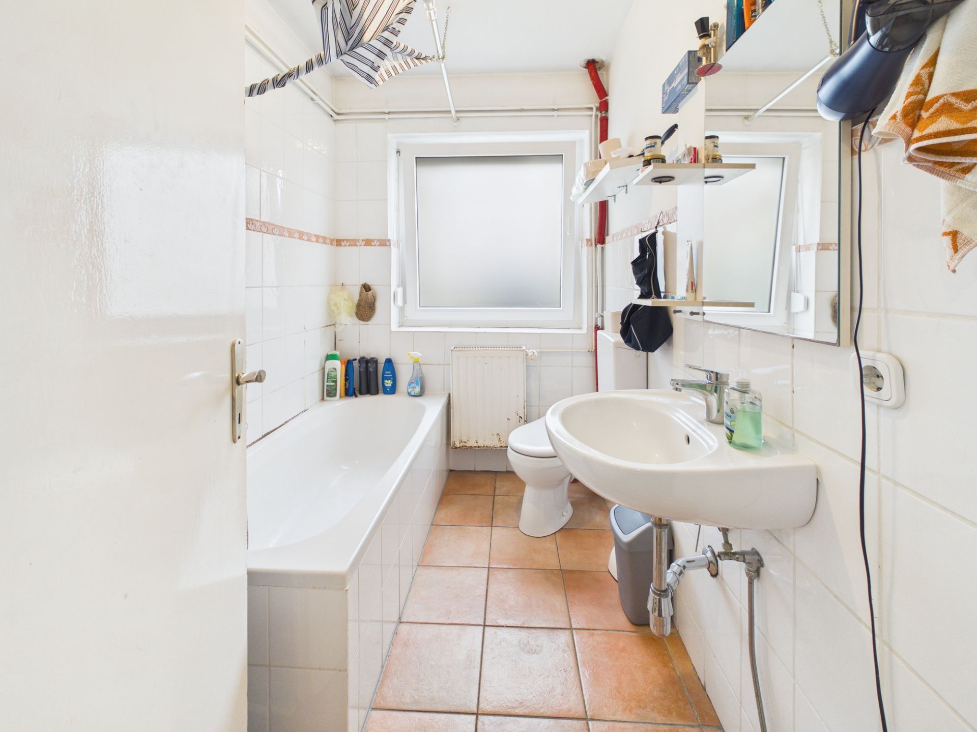 Helles Badezimmer mit Badewanne, Waschbecken, WC, Fenster und Fliesenboden.