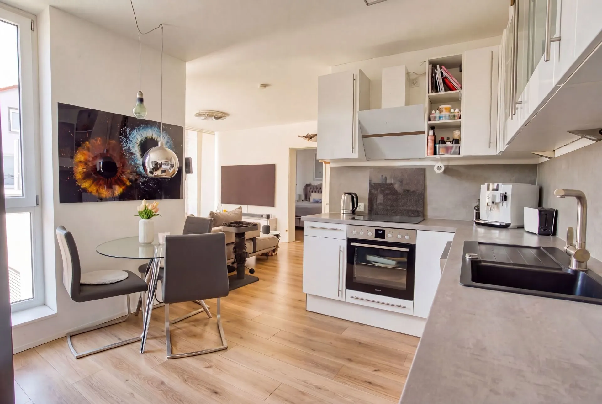 Moderne offene Küche mit Esstisch, zwei Stühlen und Blick ins Wohnzimmer mit Sofa.