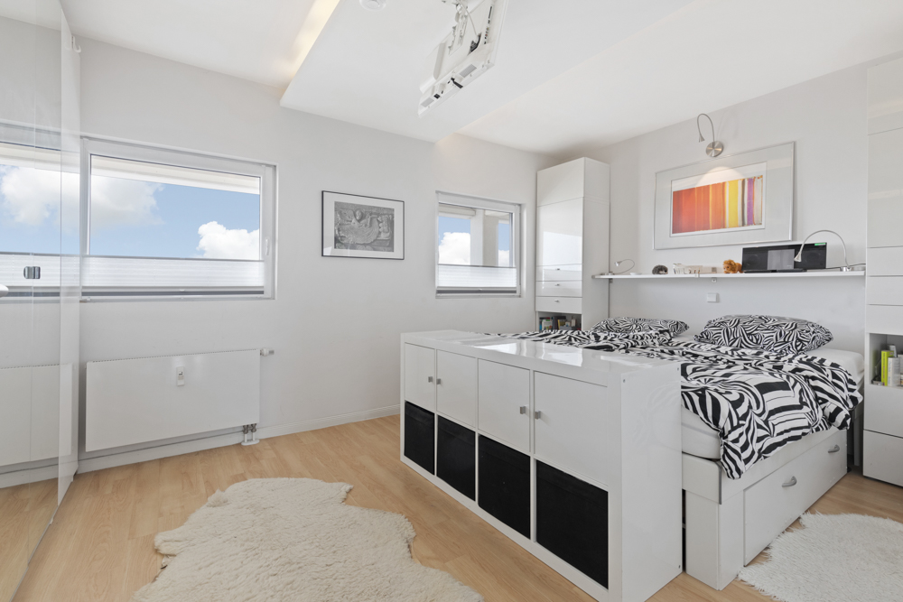 Helles Schlafzimmer mit zwei Betten, weißen Möbeln, Holzfußboden und großen Fenstern.