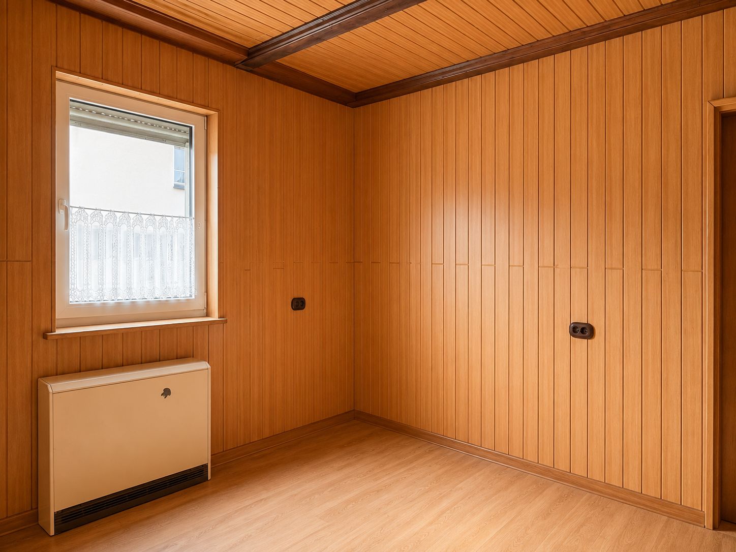 Leerer Raum mit Holzverkleidung, Fenster, Decke und Heizkörper.