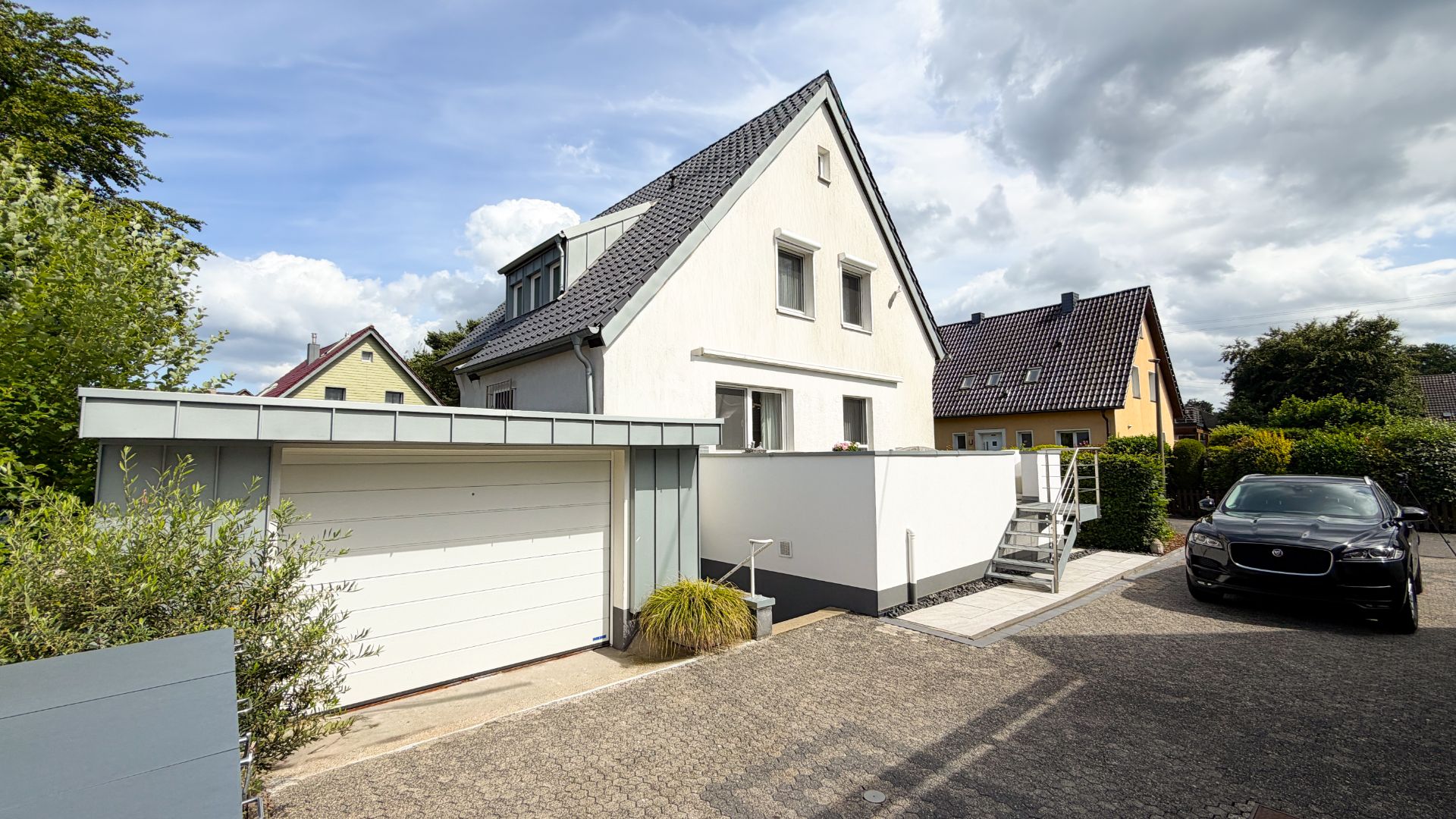 Weißes Einfamilienhaus mit Garage, Treppe und geparktem Auto davor.