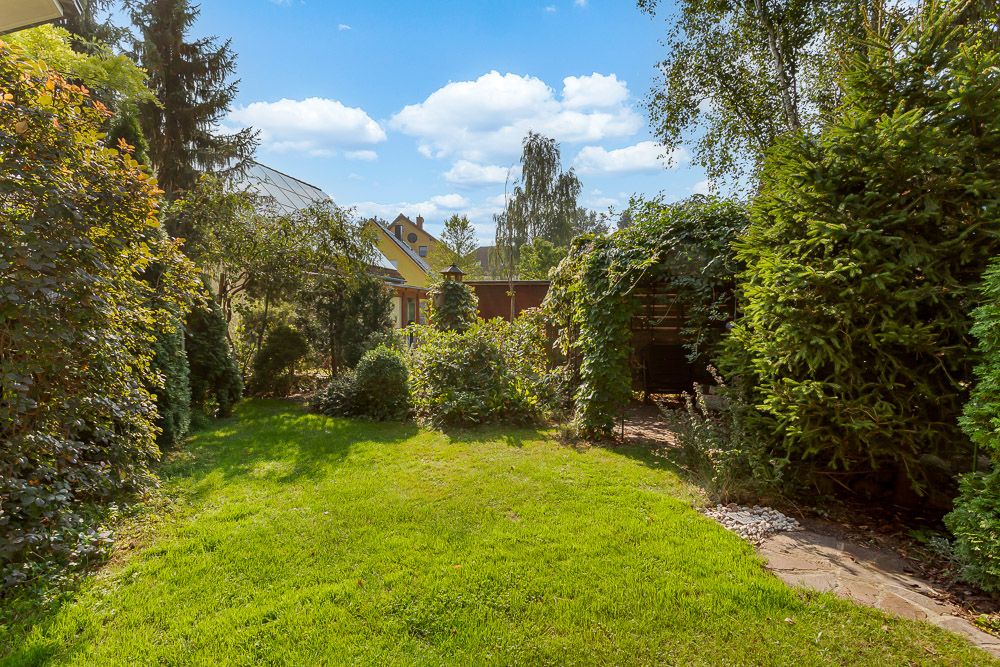 Grüner Garten mit Rasen, Bäumen, Sträuchern und einem kleinen Weg an der Seite.