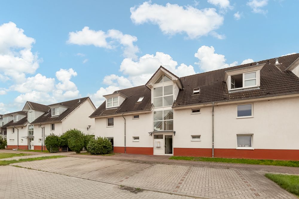 Mehrfamilienhaus mit drei Etagen, roten Sockeln und giebelförmigen Fenstern, davor Parkplätze.