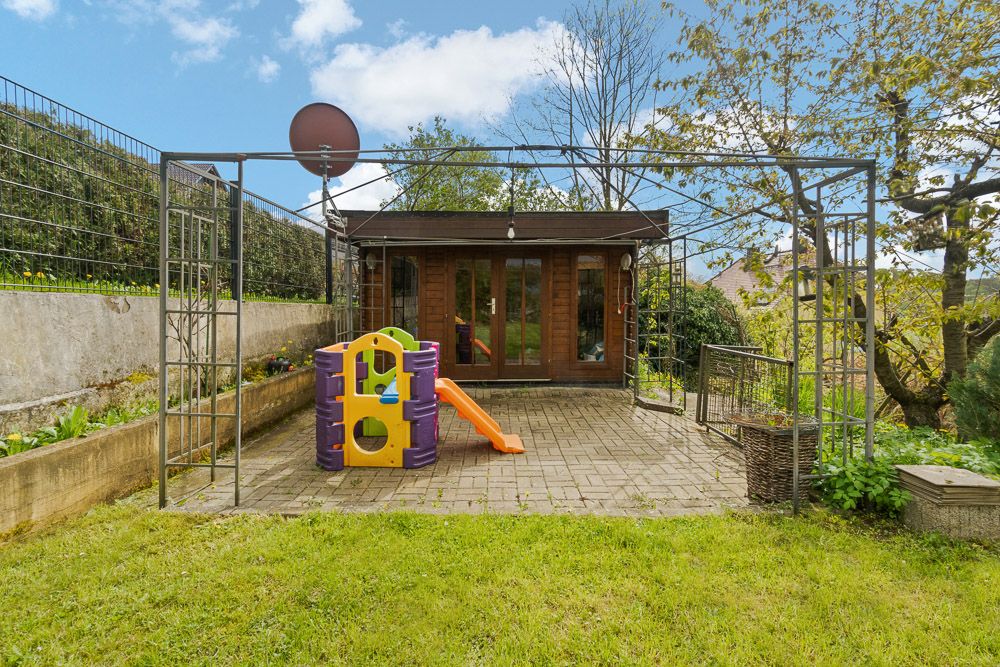 Garten mit Rasenfläche, bunter Kinderrutsche und kleinem Holzhaus im Hintergrund.