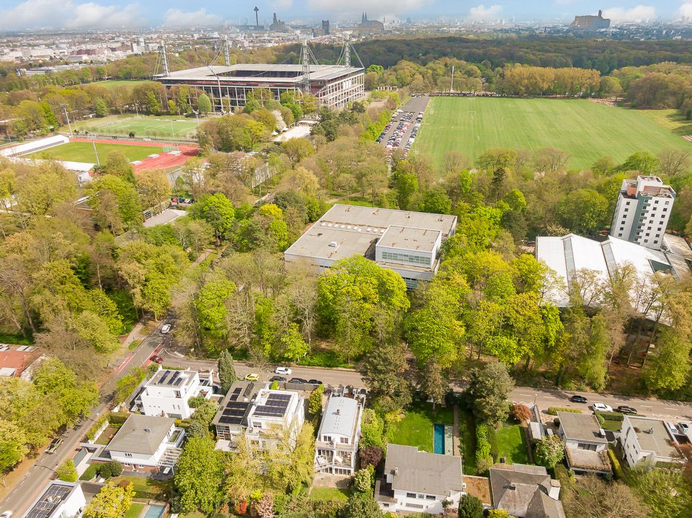 Luftaufnahme von Wohnhäusern neben einem großen Park und einem Stadion im Hintergrund.