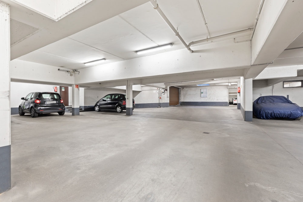 Helle Tiefgarage mit drei geparkten Autos, darunter ein Auto mit Abdeckung.