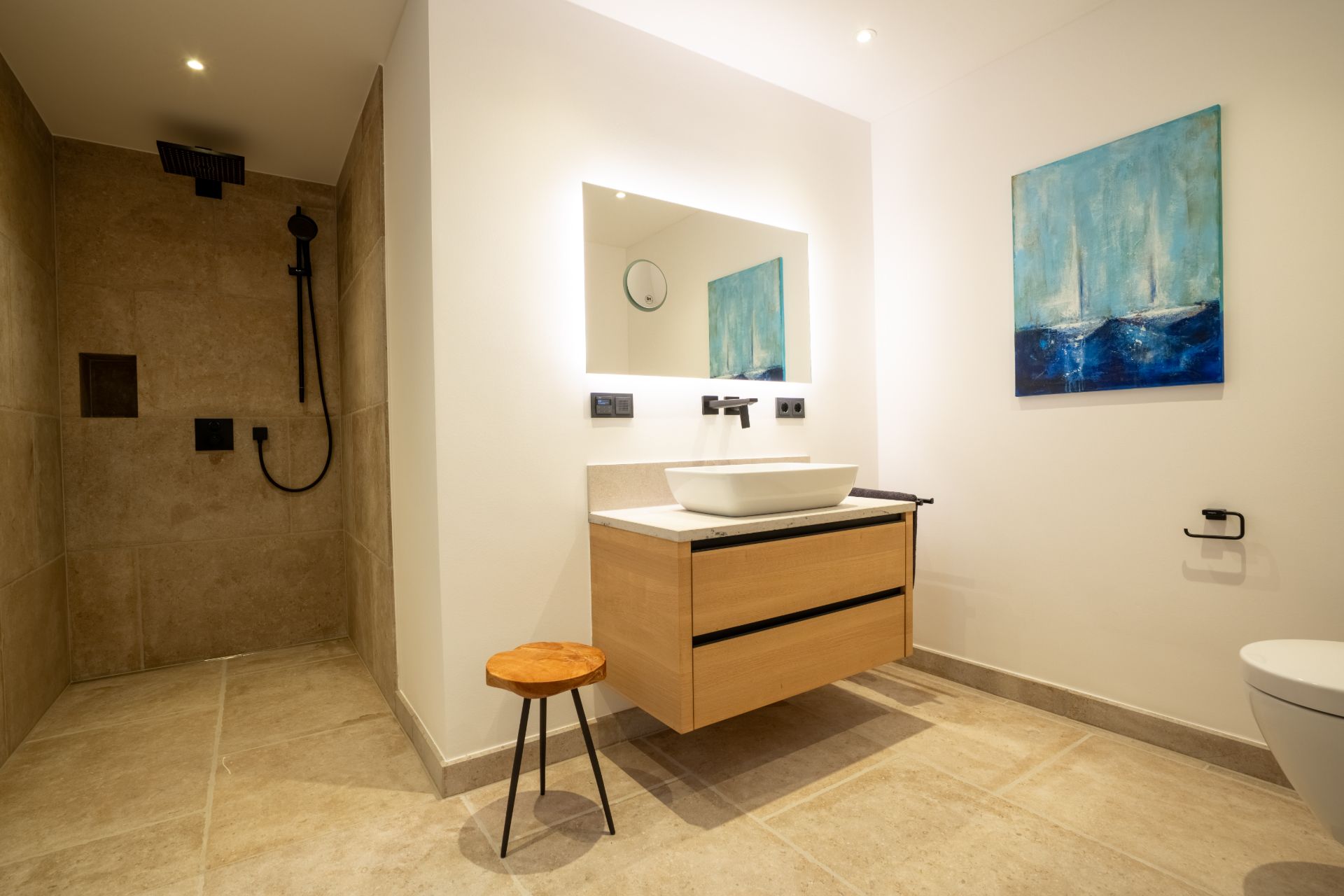 Modernes Badezimmer mit begehbarer Dusche, Waschbecken, Spiegel, Hocker und Wandbild.
