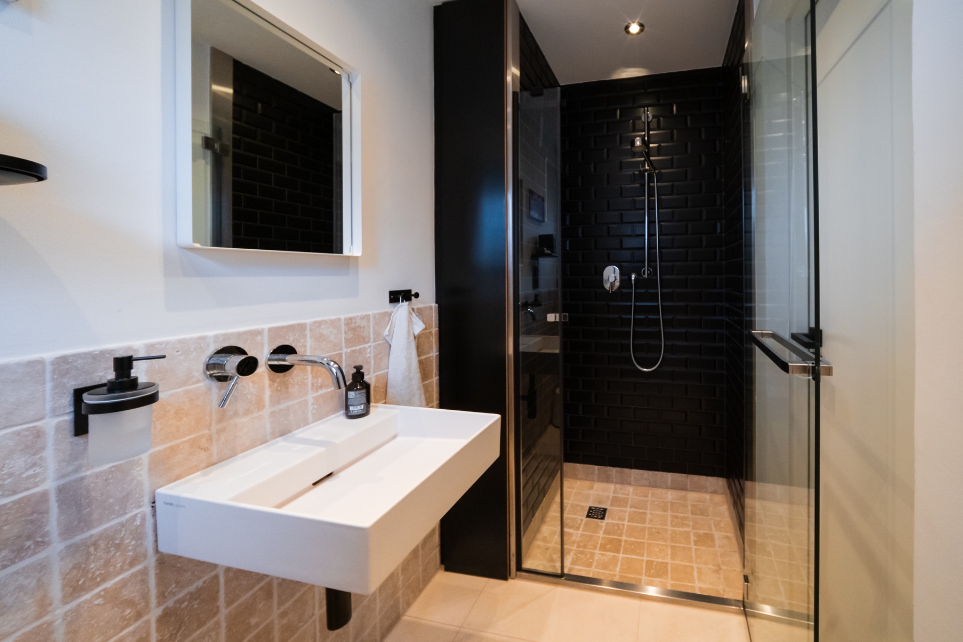 Modernes Badezimmer mit Waschtisch, Spiegel und begehbarer Dusche mit schwarzer Fliesenwand.