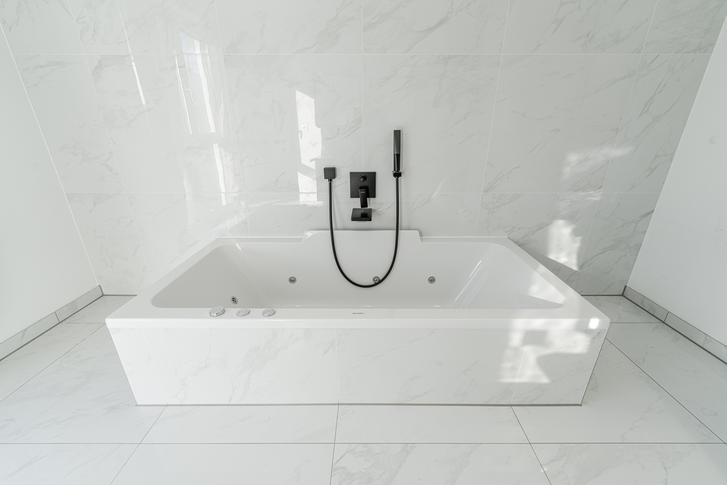 Moderne weiße Badewanne mit Marmorfliesen und schwarzer Armatur.