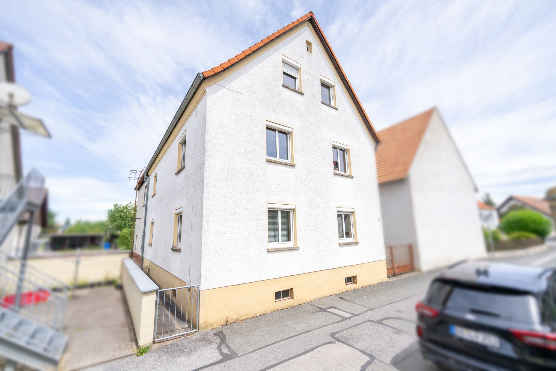 Weißes Wohnhaus mit Satteldach, mehreren Fenstern und geparktem Auto davor.