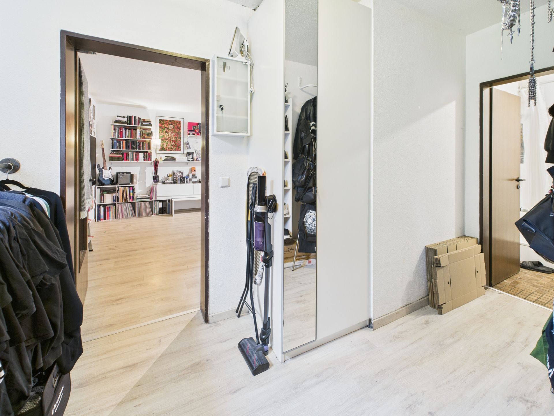 Heller Flur mit Spiegel-Garderobe, Staubsauger und Blick ins Wohnzimmer mit Bücherregal.
