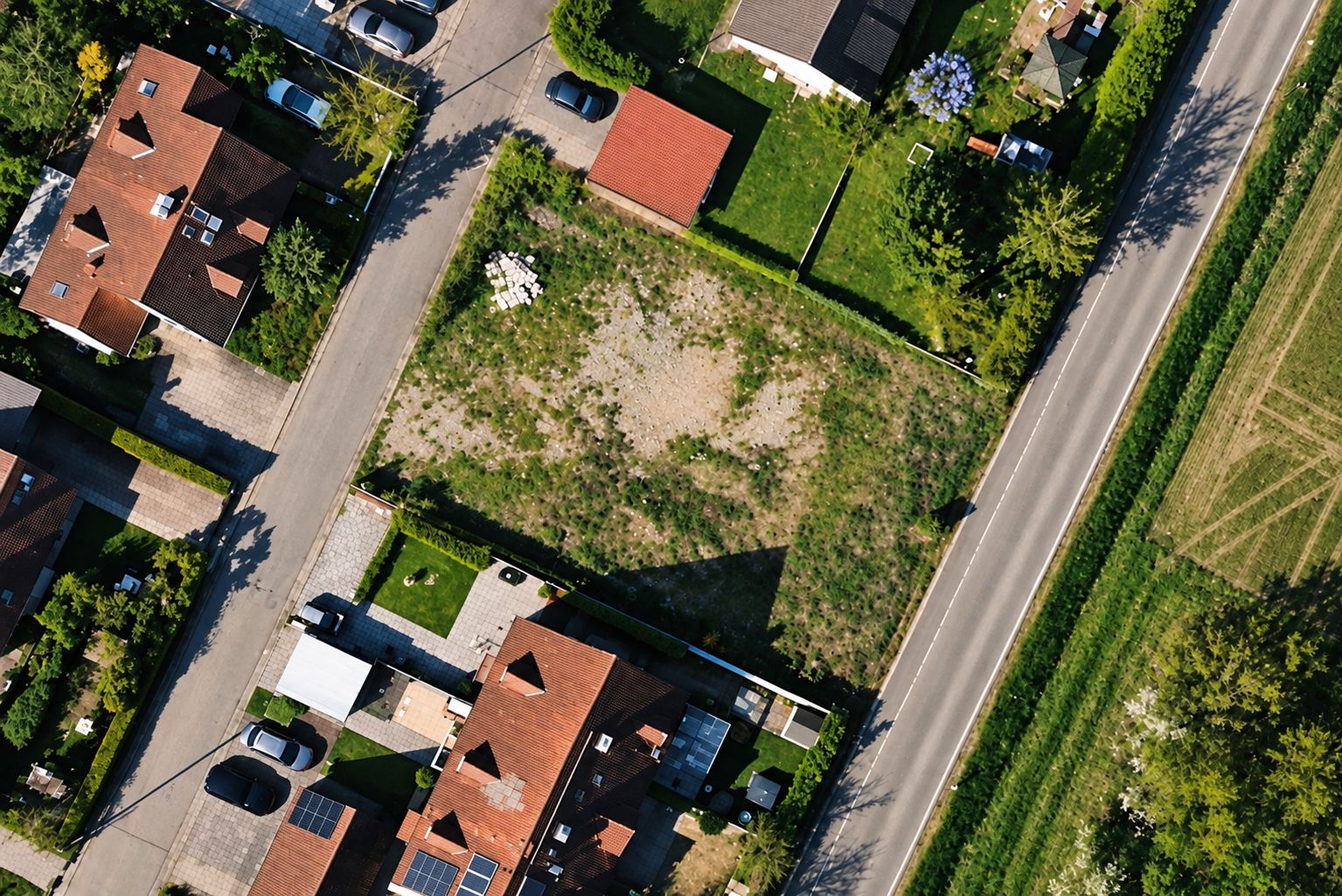 Luftaufnahme eines leeren Grundstücks zwischen Wohnhäusern an einer Straße.