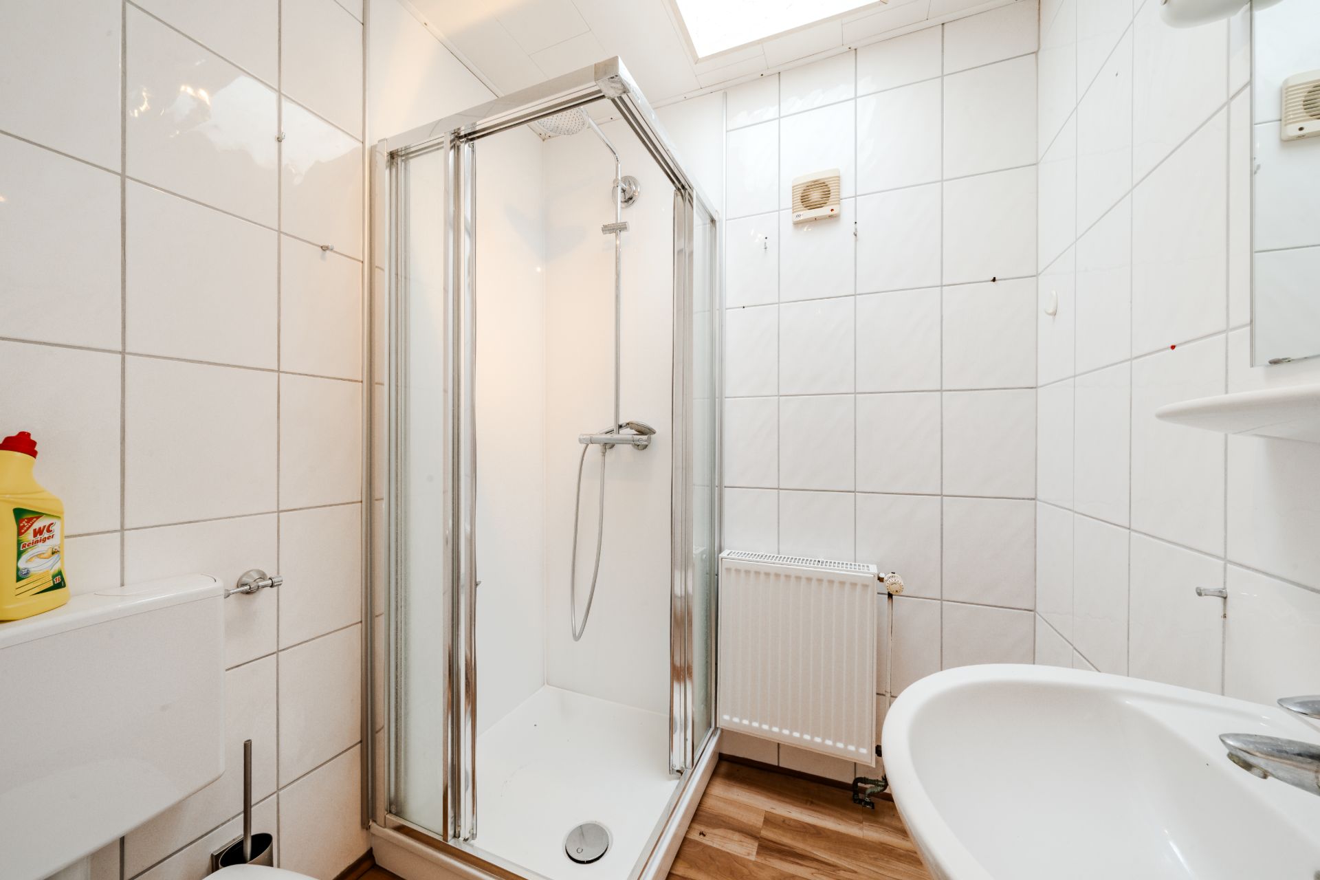 Modernes Badezimmer mit Duschkabine, Waschbecken, Heizung und weißen Fliesen.