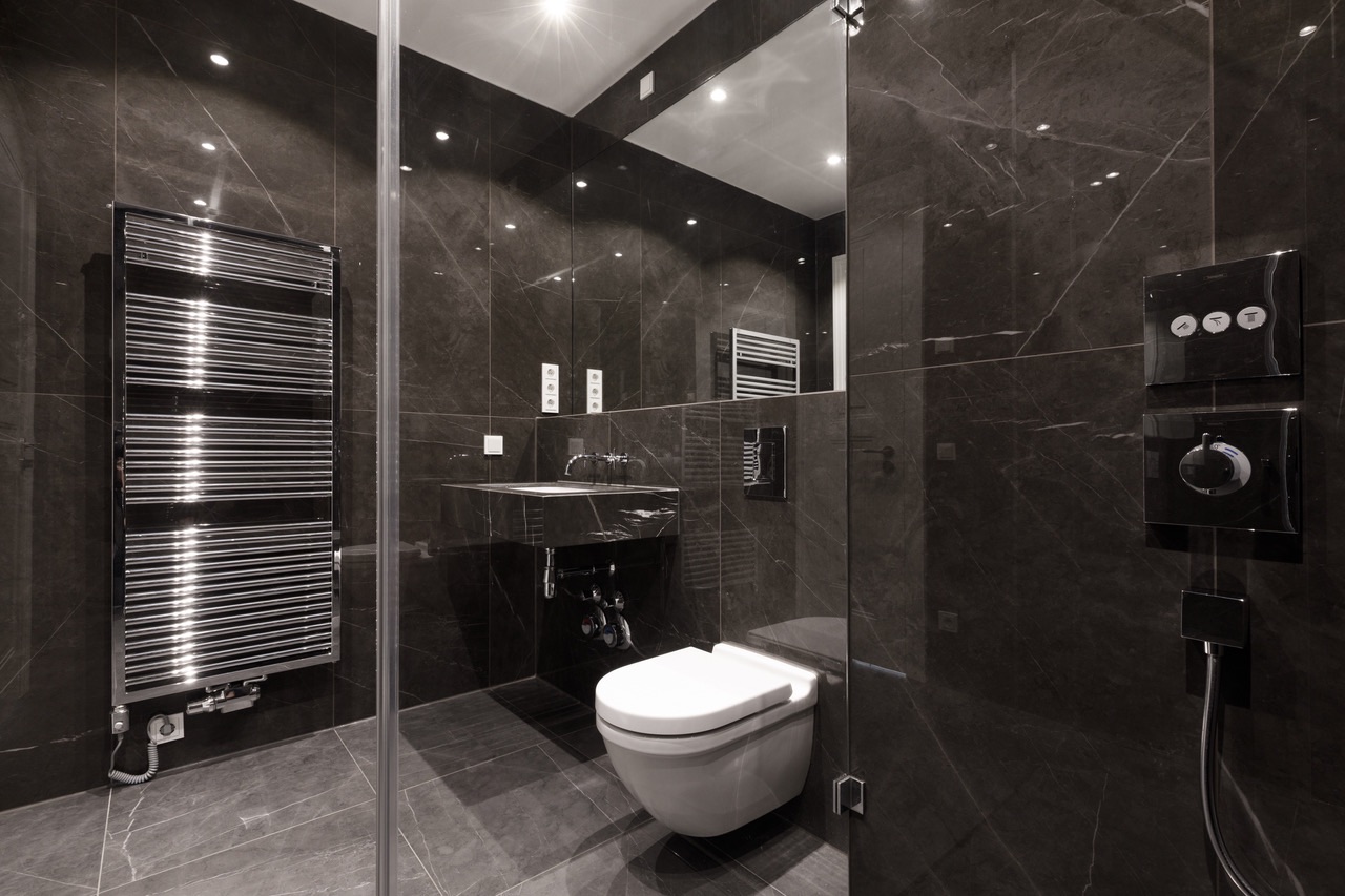 Modernes Badezimmer mit dunklen Fliesen, Wandtoilette, Waschbecken und Handtuchheizkörper.