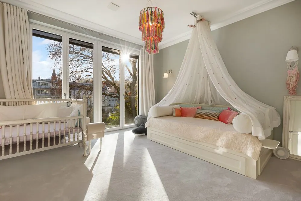 Helles Kinderzimmer mit großem Fenster, Babybett und Tagesbett mit Baldachin.