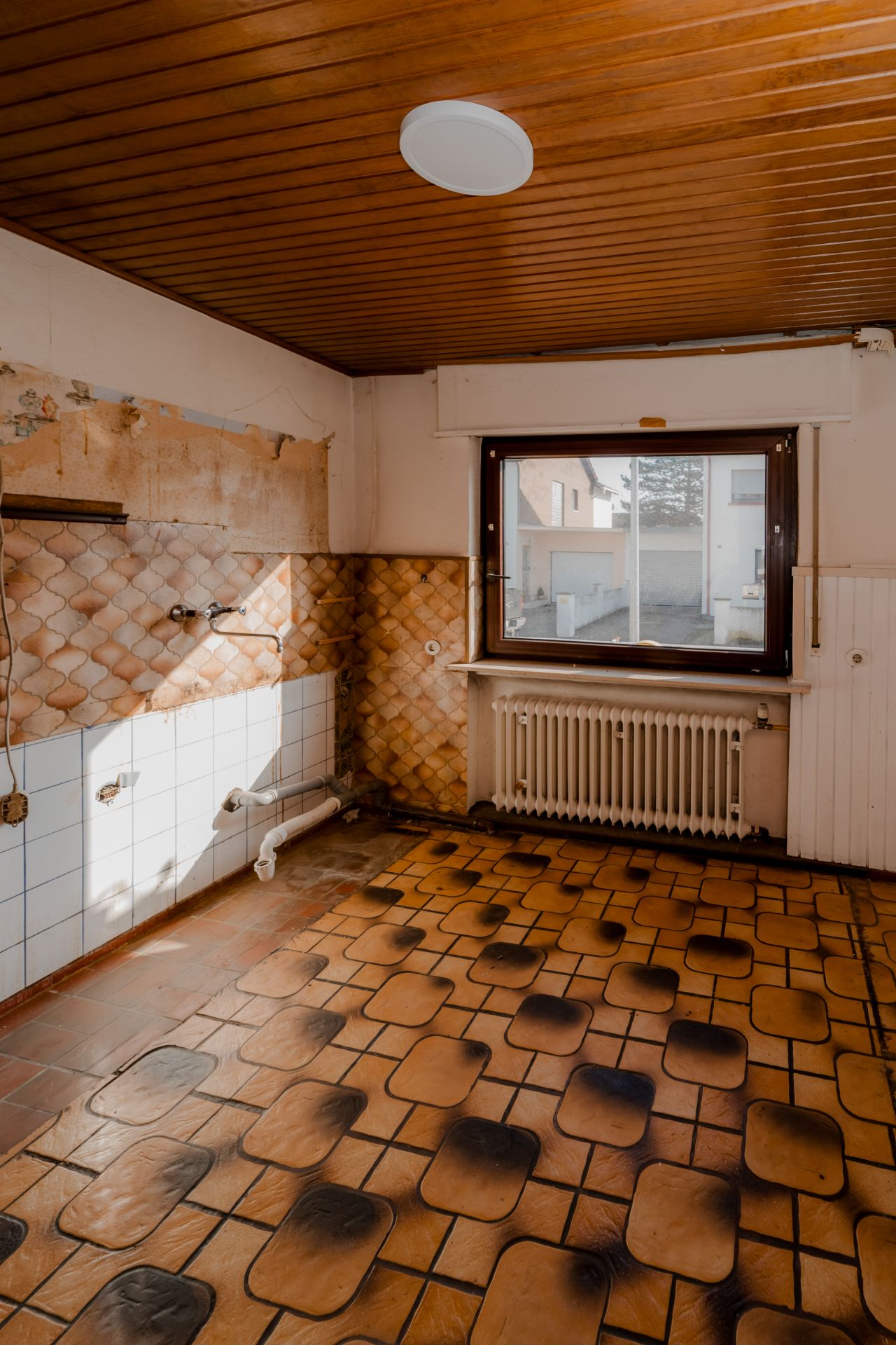 Leerer Raum mit gemustertem Fliesenboden, brauner Holzdecke und großem Fenster.