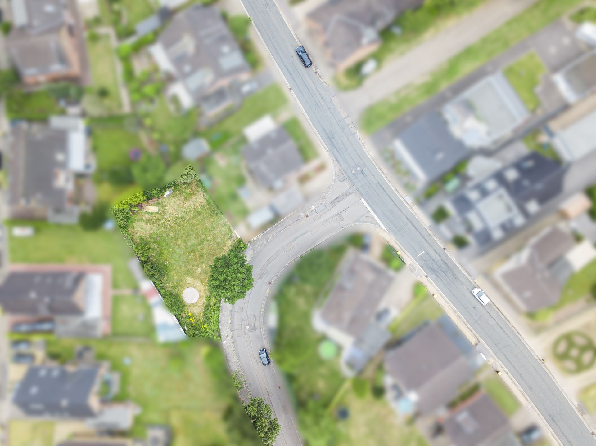 Luftaufnahme eines leeren Grundstücks an einer Straßenecke in einem Wohngebiet.