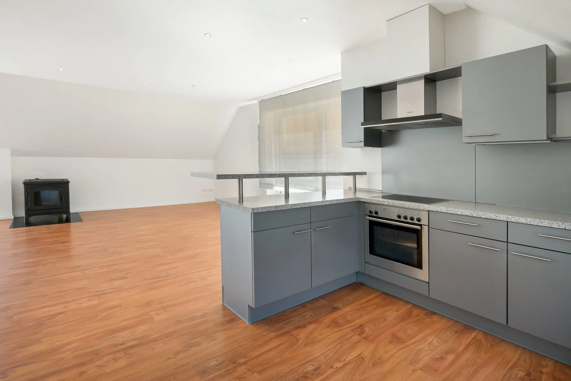 Moderne Einbauküche mit grauen Schränken und Holzfußboden in einem offenen Wohnraum.