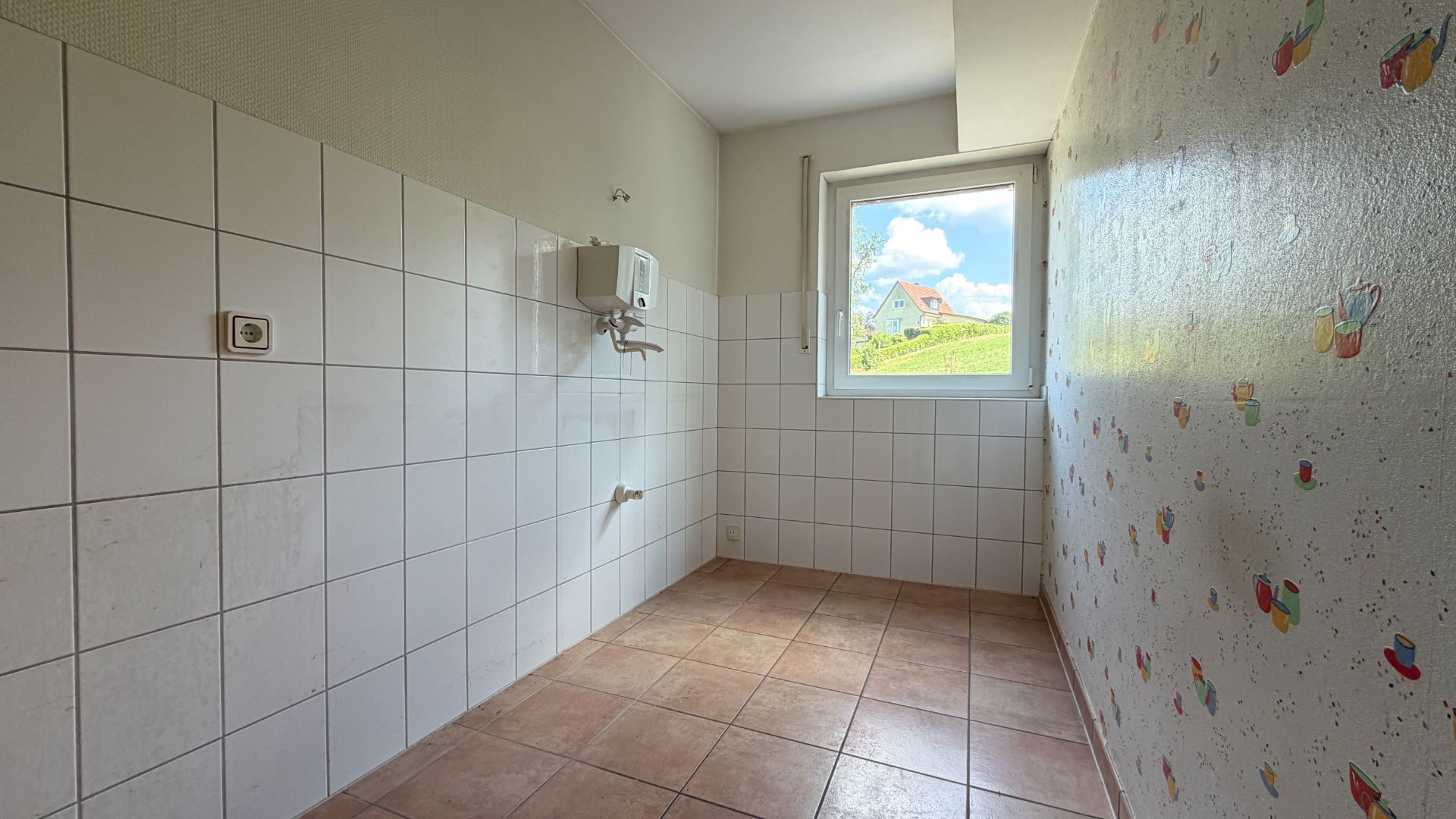 Leerer, gefliester Raum mit Fenster und bunter Tapete auf einer Wand.