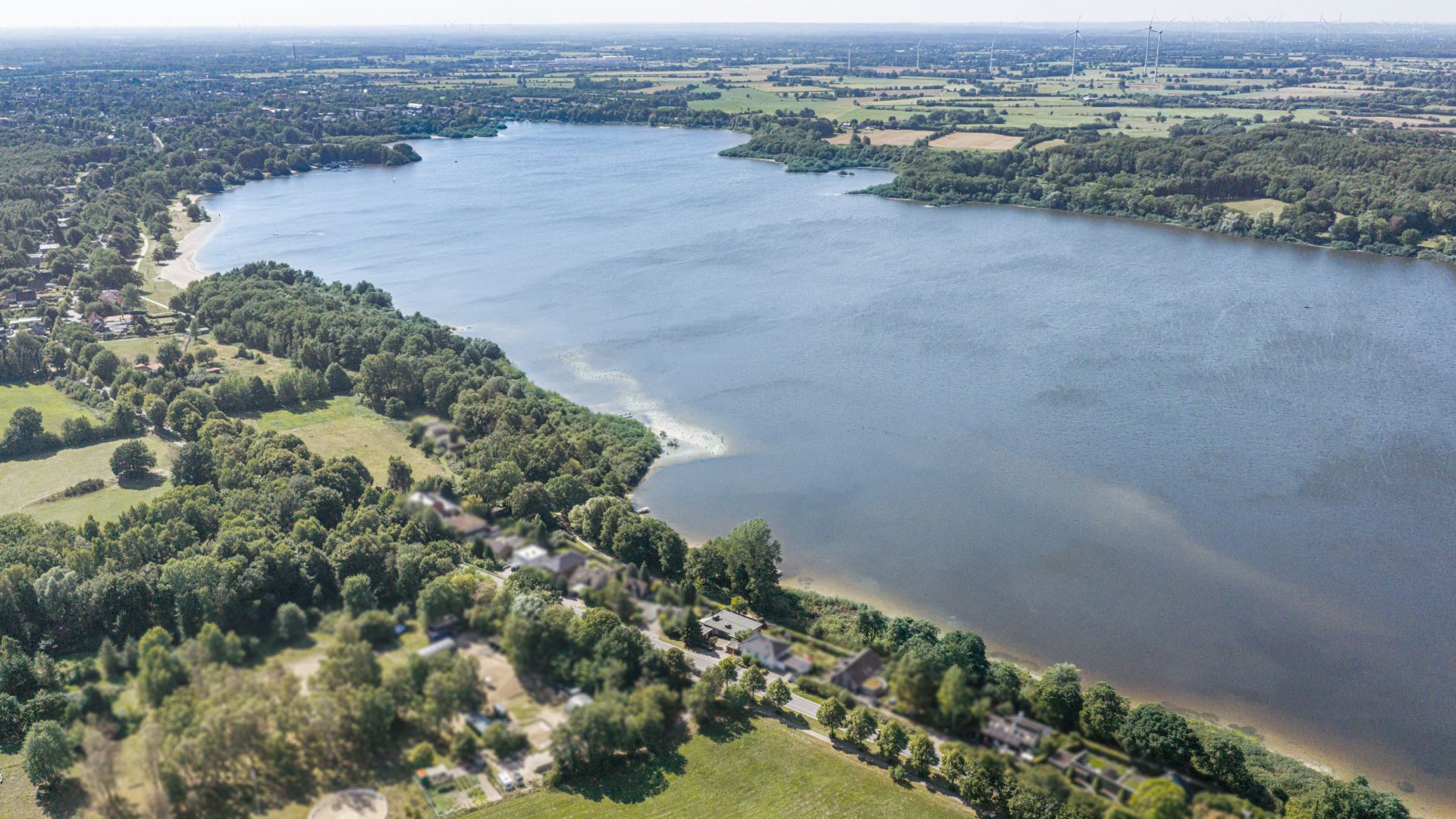 Luftaufnahme von einem großen See mit Bäumen und Häusern am Ufer.