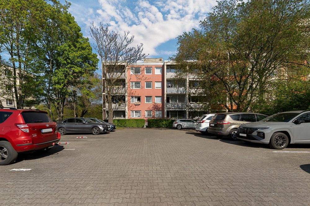 Mehrere Autos parken auf einem Parkplatz vor einem Wohngebäude mit Balkonen.