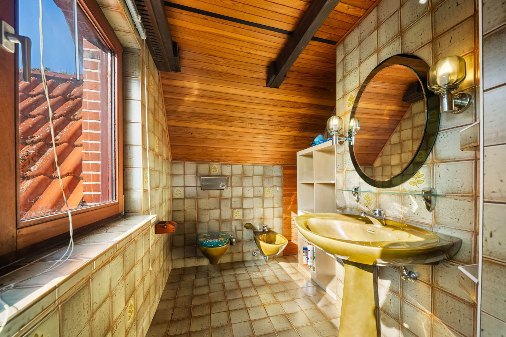 Badezimmer mit gelbem Waschbecken, WC, Bidet, Wandspiegel und Holzdecke unter Dachschräge.