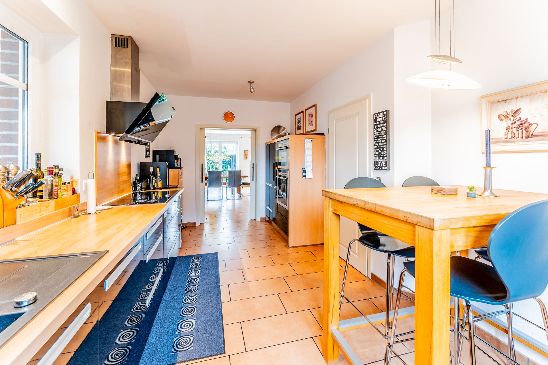 Helle Küche mit Holzarbeitsplatte, Esstisch, Stühlen und Geräten, Blick in Esszimmer.