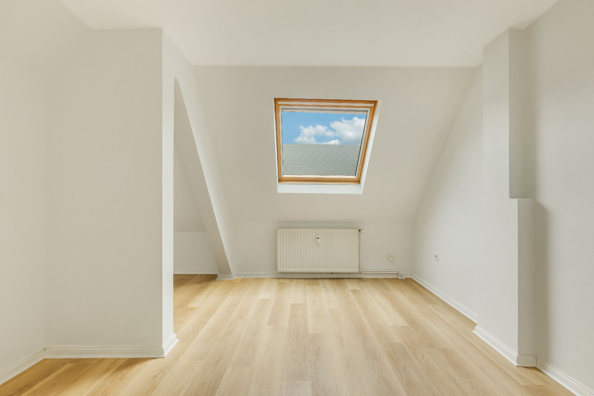 Leerer, heller Raum mit schräger Decke, Dachfenster und hellem Holzfußboden.