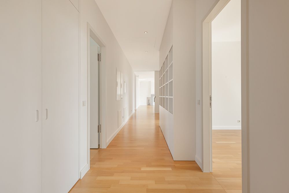 Heller Flur mit Holzboden, weißen Wänden, Türen und eingebauten Regalen.