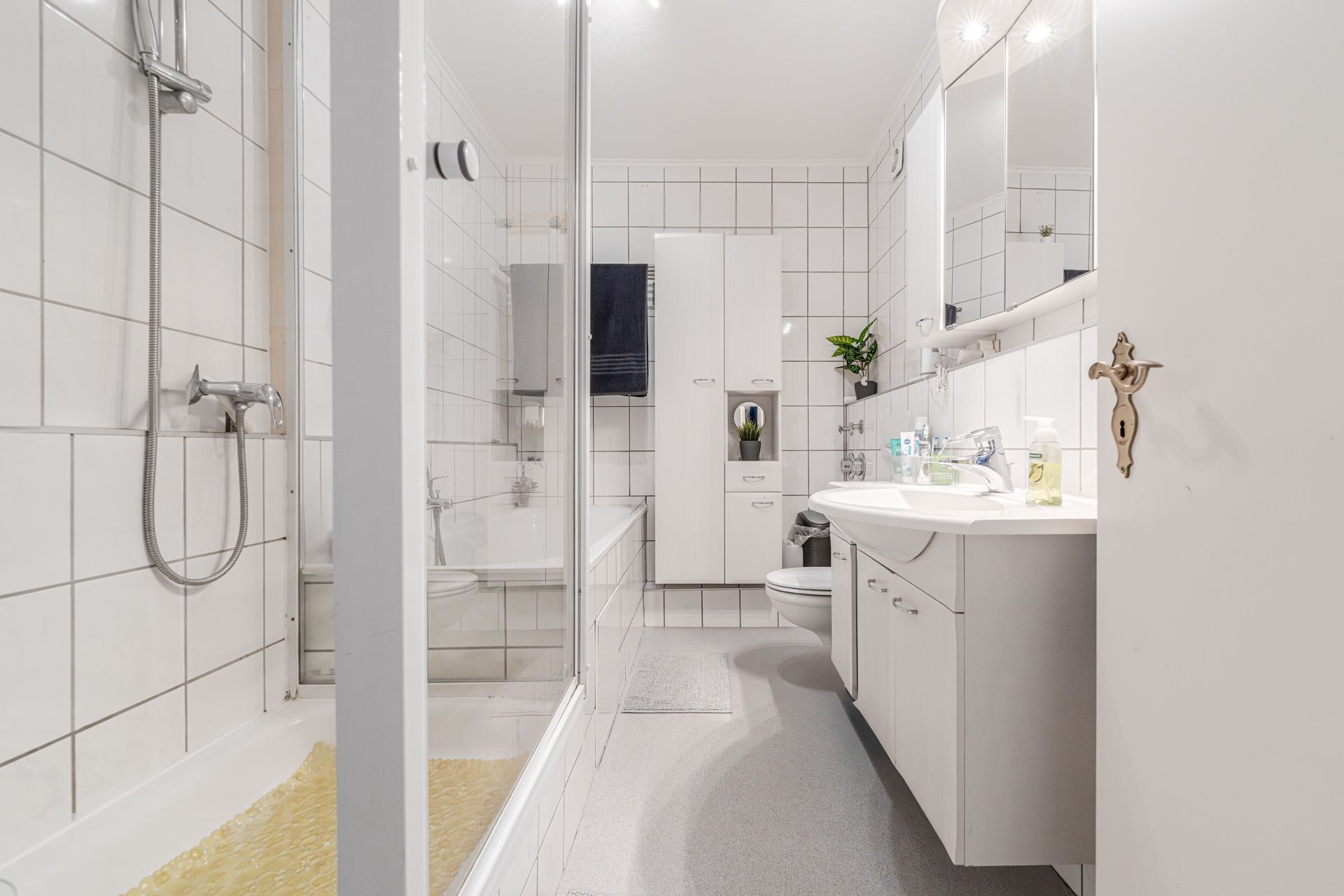 Helles Badezimmer mit Badewanne, Dusche, Waschbecken, Spiegel und weißen Fliesen.