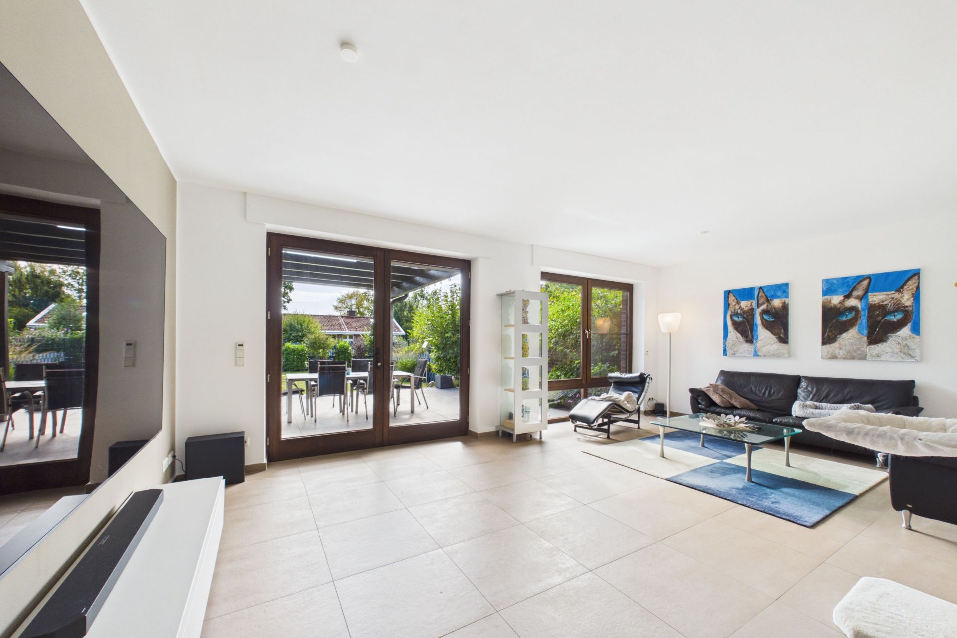 Helles Wohnzimmer mit großer Fensterfront, Sofa, Glastisch und Zugang zur Terrasse.