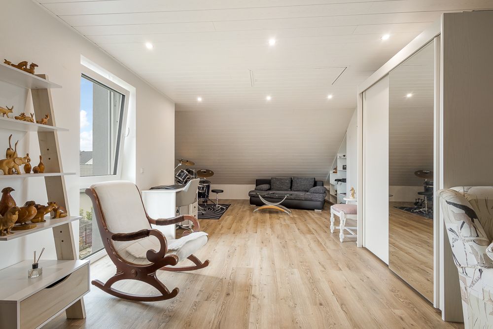 Helles Dachzimmer mit Schaukelstuhl, Sofa, Regal und großem Spiegel an der Wand.