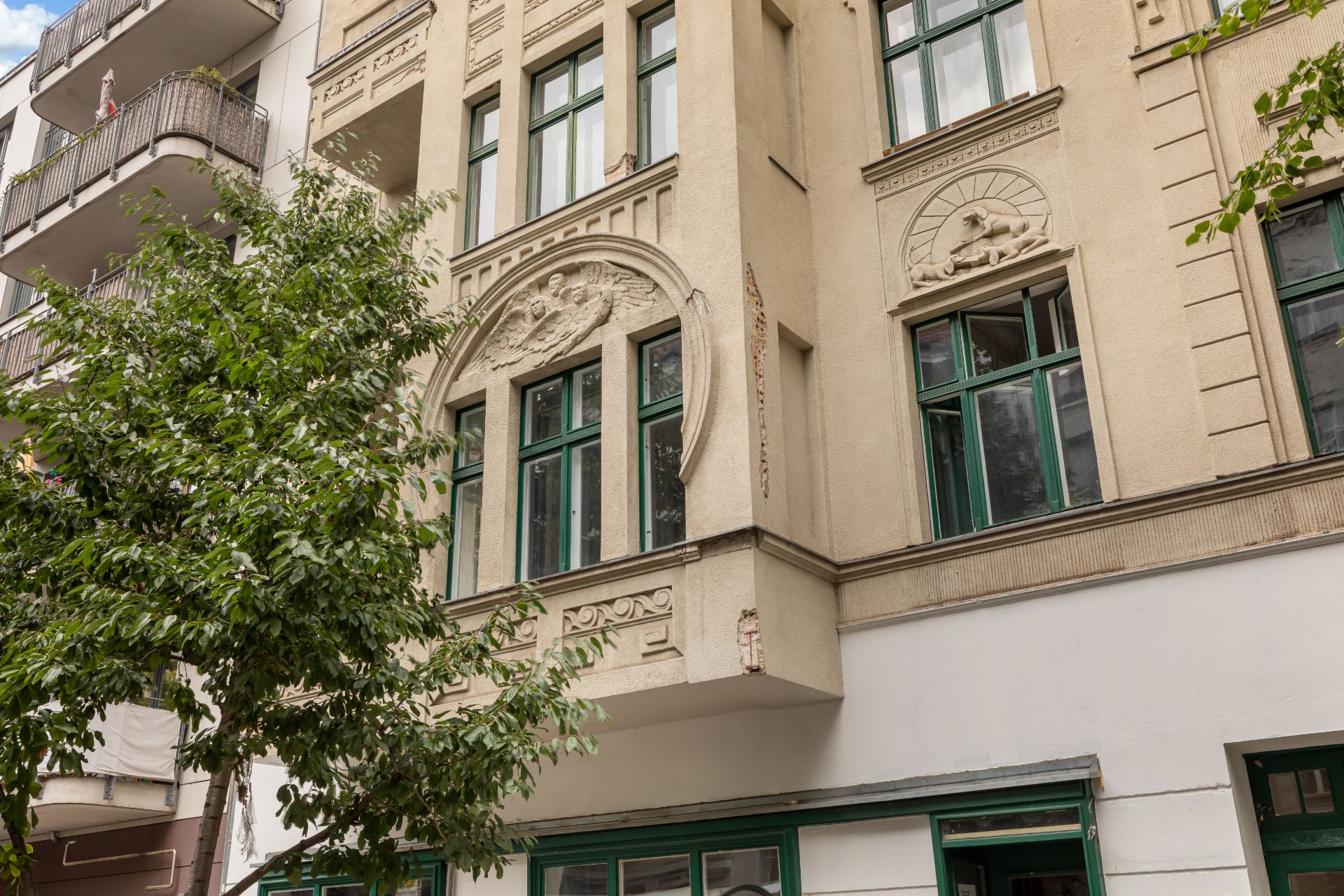 Fassade eines Wohnhauses mit grünen Fenstern und dekorativen Stuckverzierungen.