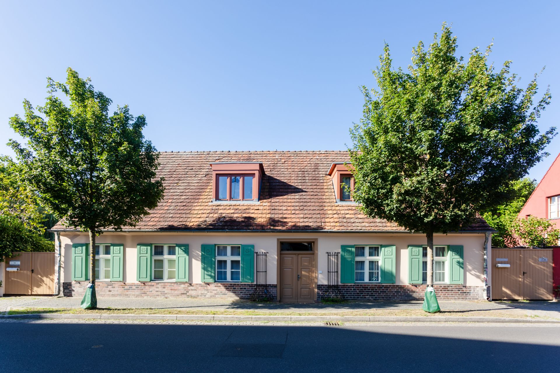 Einfamilienhaus mit grünem Fensterläden, zwei Bäumen davor und brauner Eingangstür.