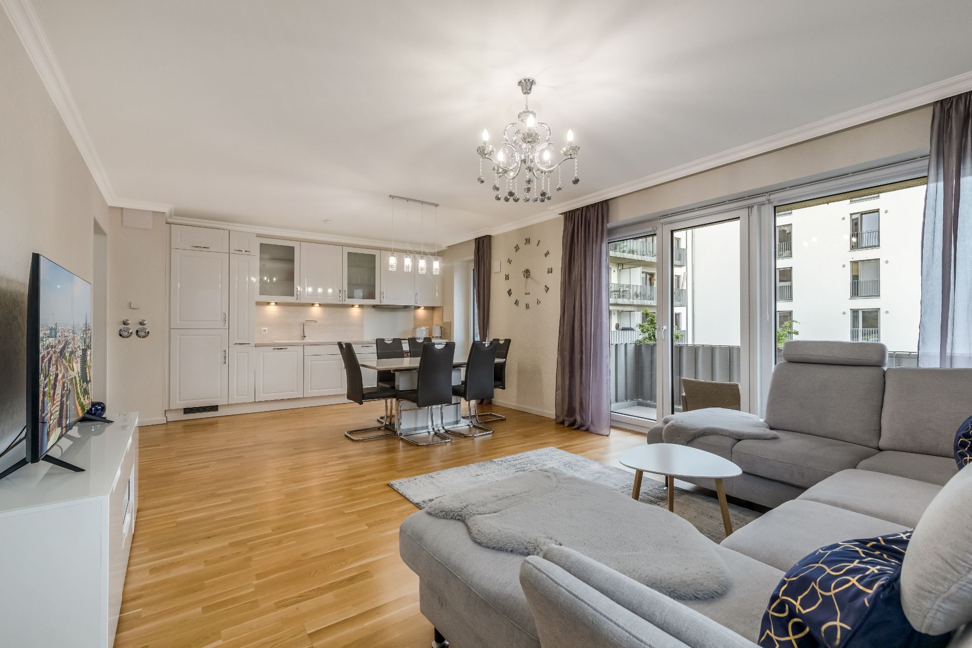 Helles Wohnzimmer mit grauem Sofa, Esstisch, offener Küche und Balkonzugang.