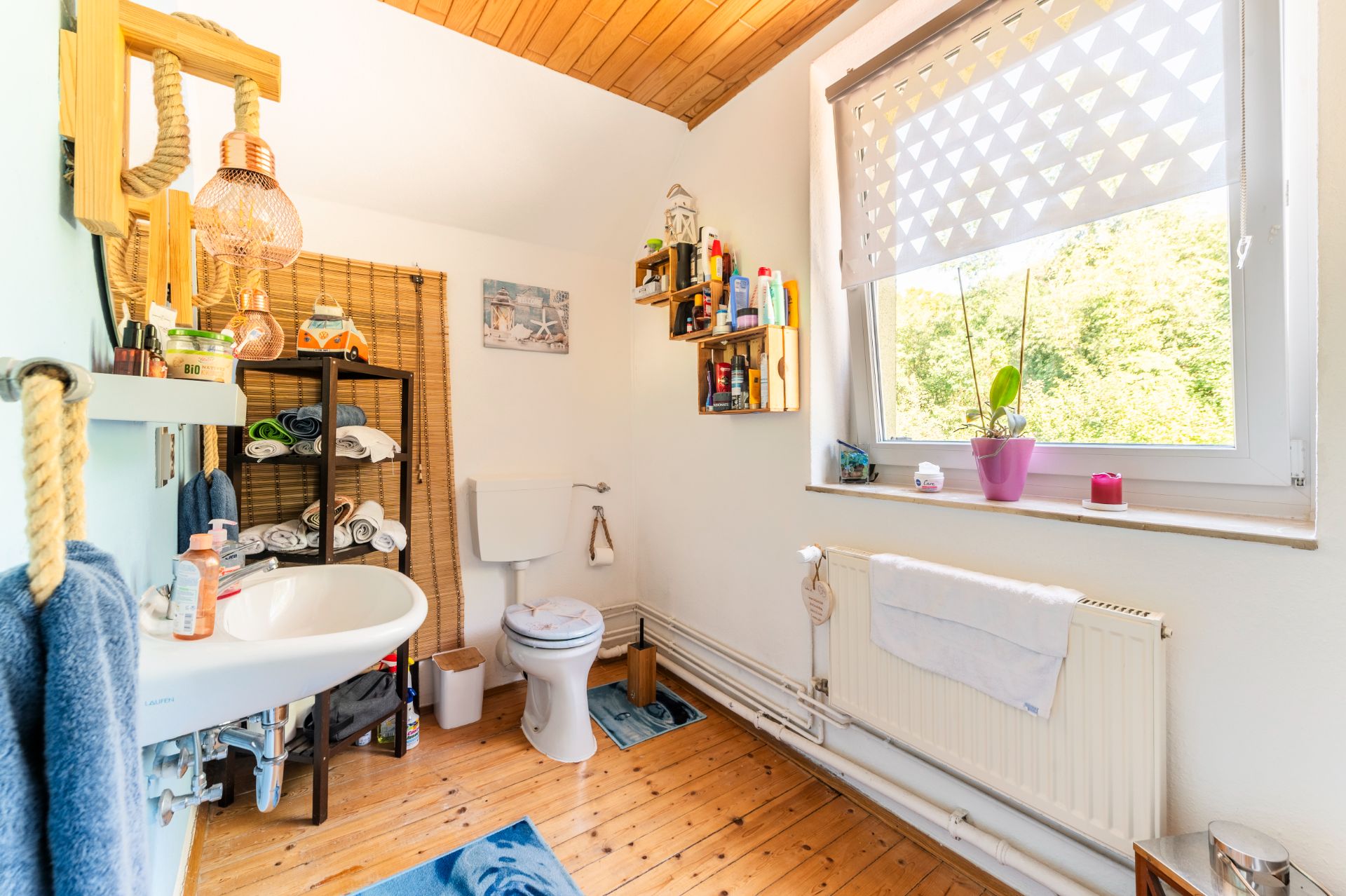 Helles Badezimmer mit Waschbecken, Toilette, Regal, Fenster und Holzboden.