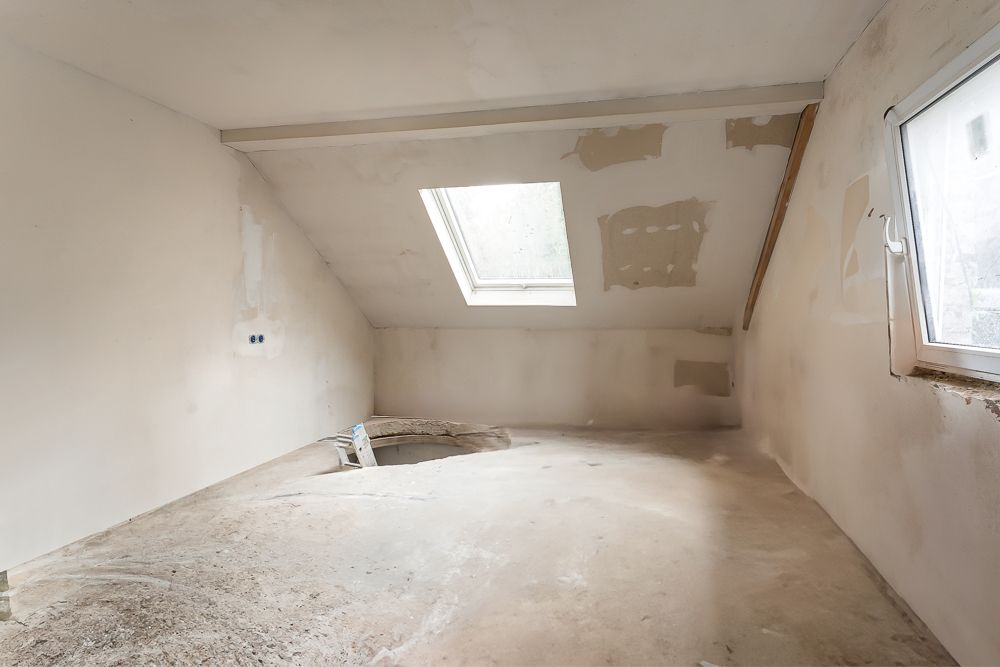 Unausgebauter Dachraum mit Dachfenster, Rohboden und sichtbaren Gipsarbeiten.