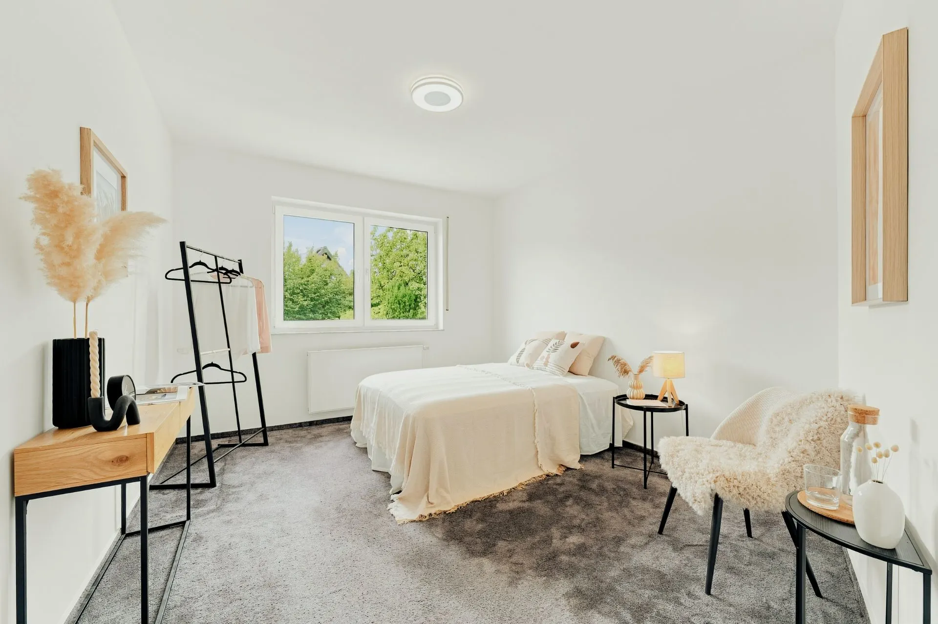 Helles Schlafzimmer mit Bett, Nachttischen, Stuhl und großem Fenster mit Blick ins Grüne.