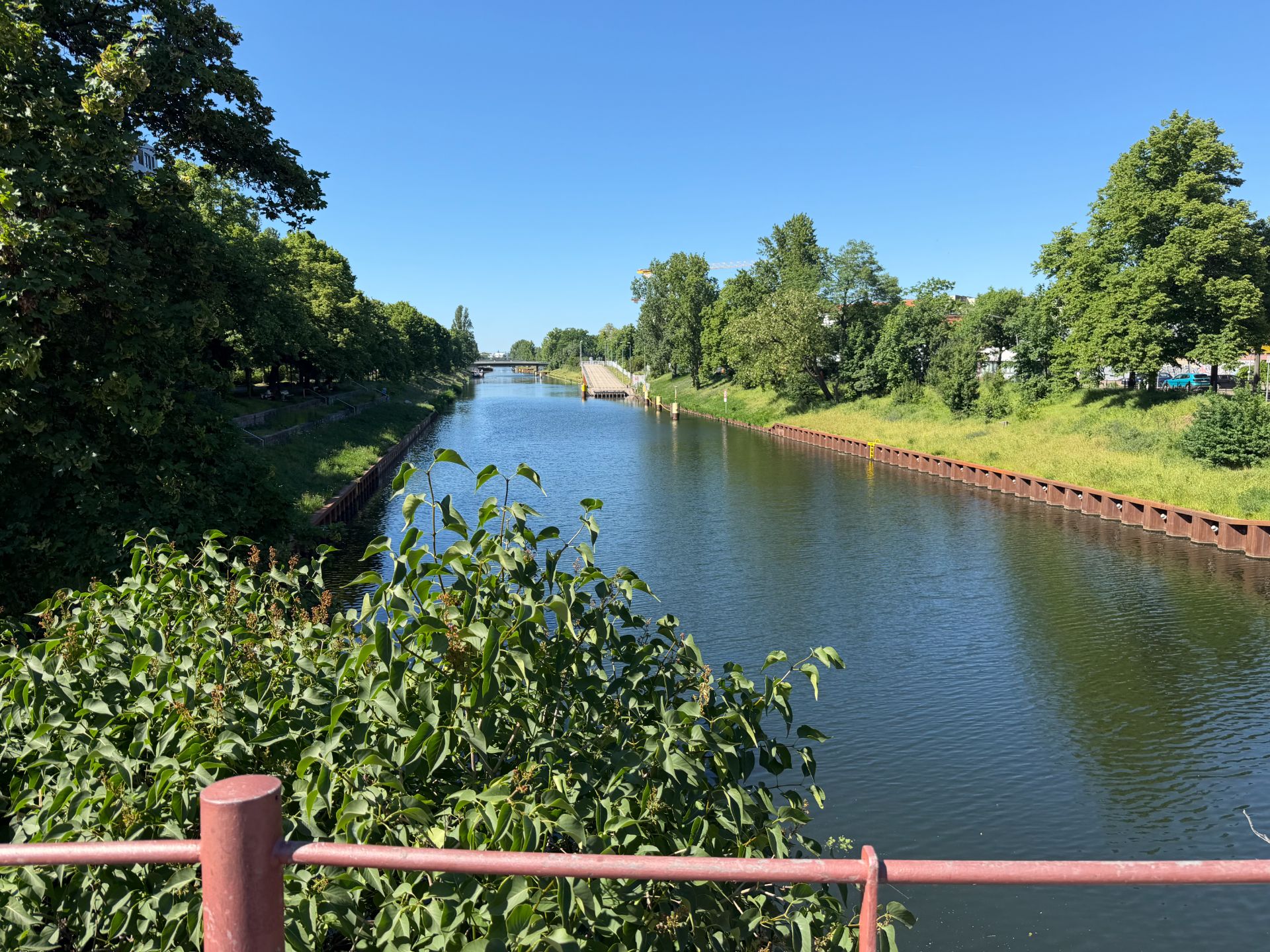 Fluss mit Uferböschungen und Bäumen, Blick von einer Brücke bei sonnigem Wetter.