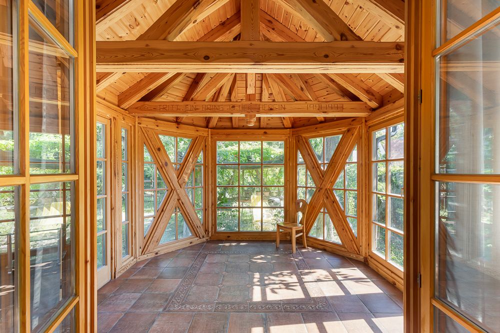 Heller Wintergarten aus Holz mit großen Fenstern und einem einzelnen Stuhl im Eck.