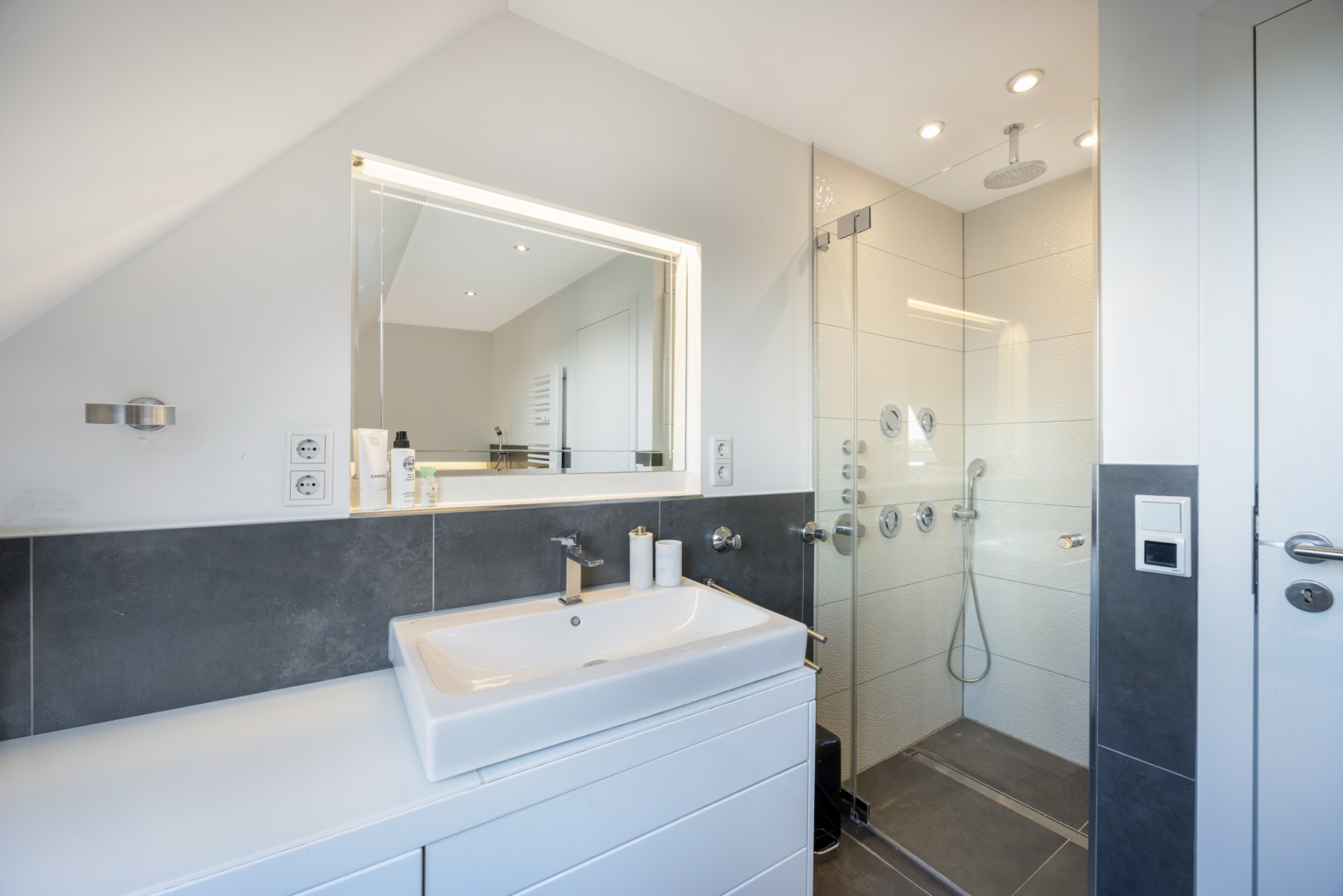 Modernes Badezimmer mit beleuchtetem Spiegel, Waschbecken und Glasdusche.