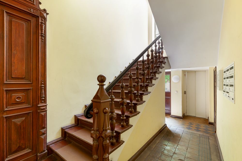 Treppenhaus mit Holztreppe, Holztür und Fliesenboden in einem Wohnhaus.