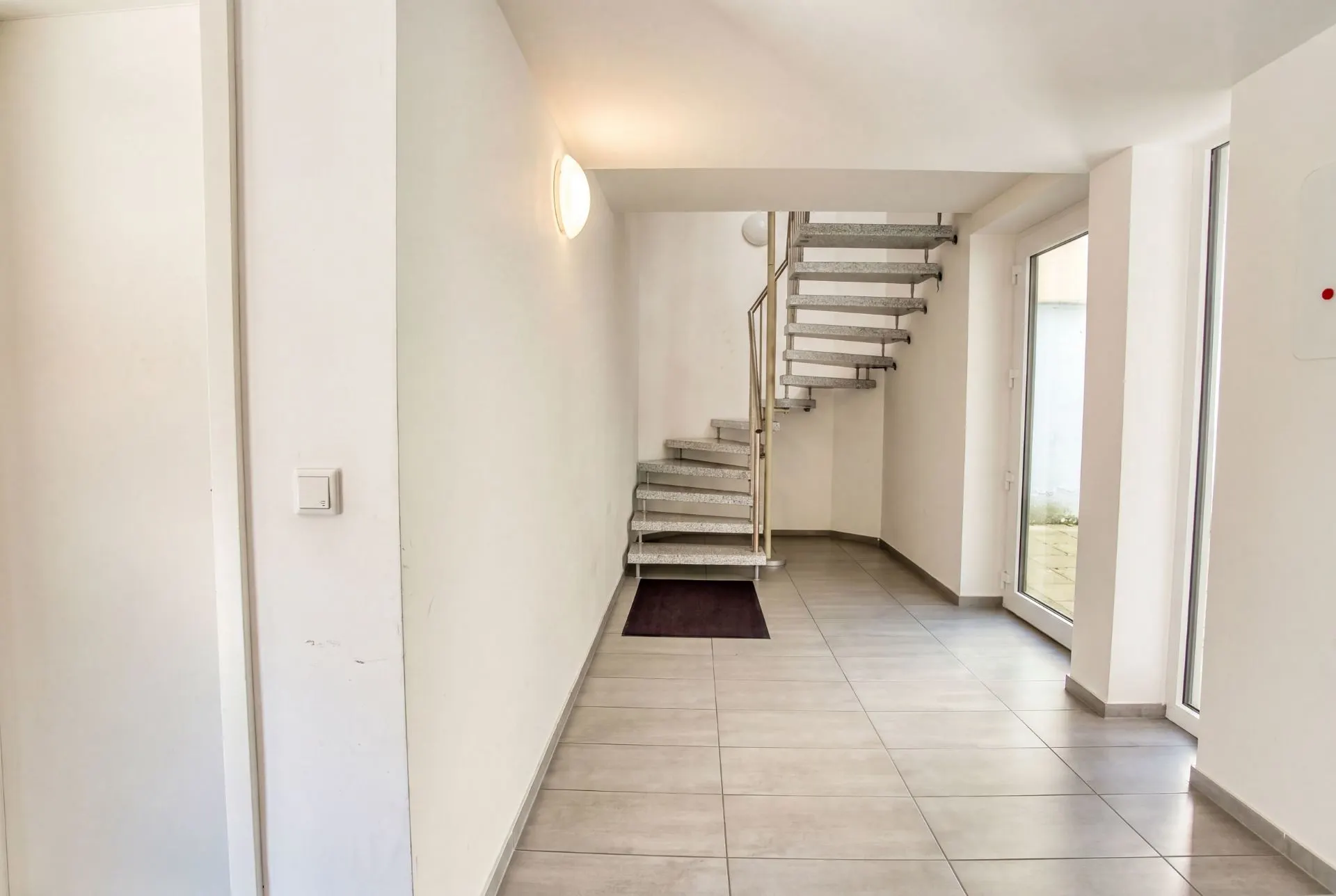 Heller Eingangsbereich mit Fliesenboden und moderner Treppe nach oben.