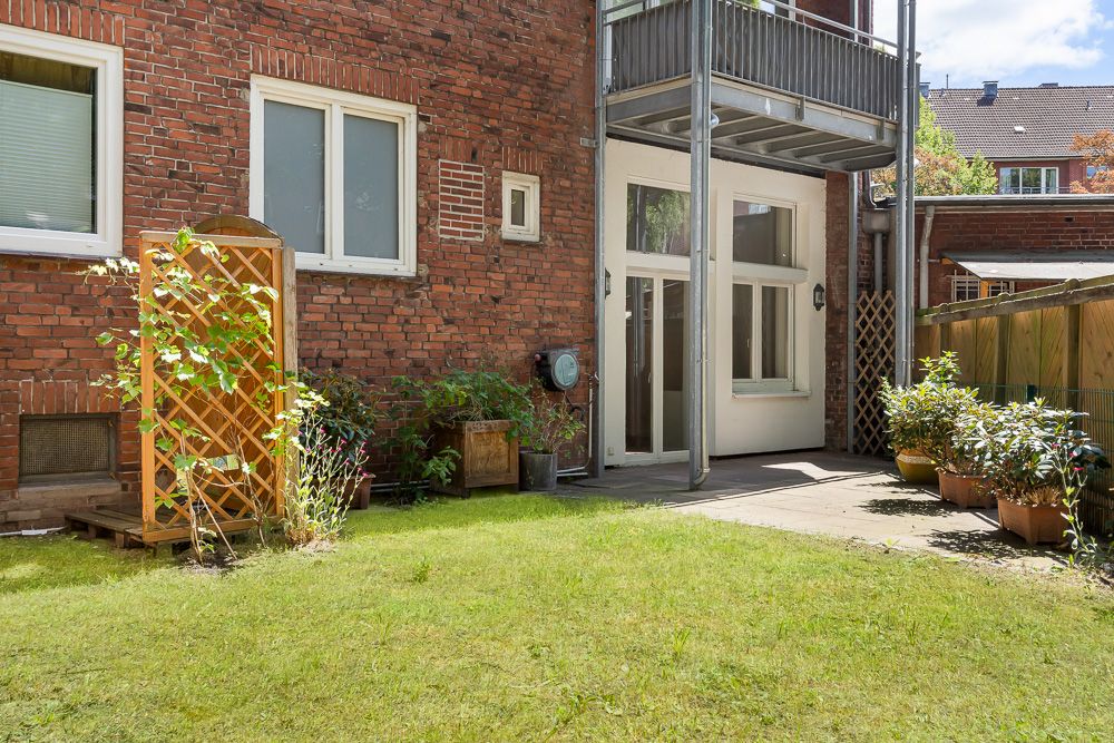 Kleiner Garten mit Rasen, Terrasse und Topfpflanzen an einem Backsteinhaus.